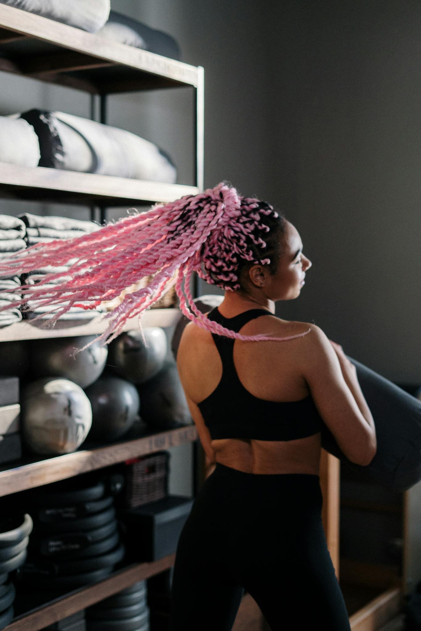 A vibrant yoga instructor with pink hair prepares for class in a modern studio setting.